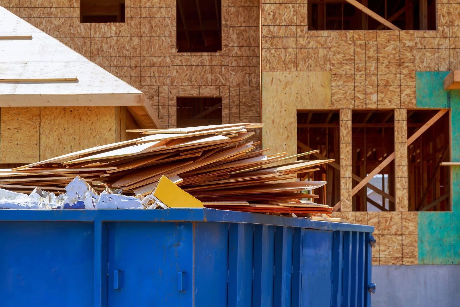 Blue roll-off dumpster collecting wood offcuts at a construction project